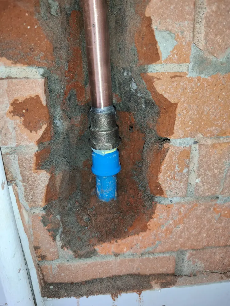 Unión de cañería de cobre con conexión azul en muro de ladrillo